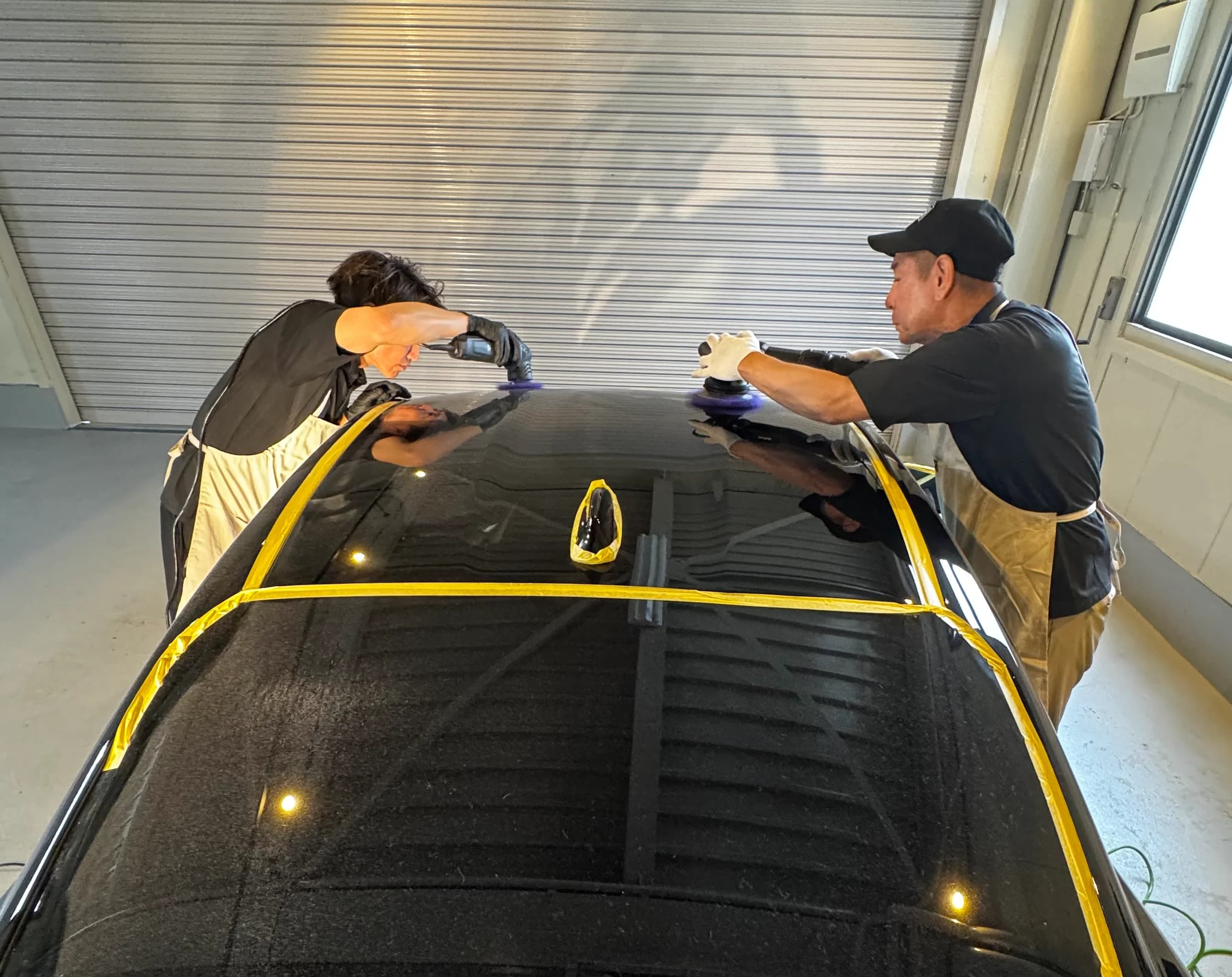 施工スタジオで黒い車を2名で研磨する様子